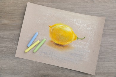 Beautiful drawing of lemon and pastels on wooden table, top view