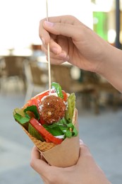 Photo of Woman eating wafer with falafel and vegetables outdoors, closeup. Street food