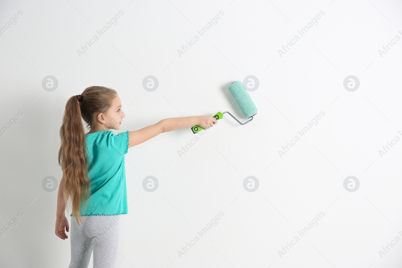 Photo of Little child painting with roller brush on white wall indoors