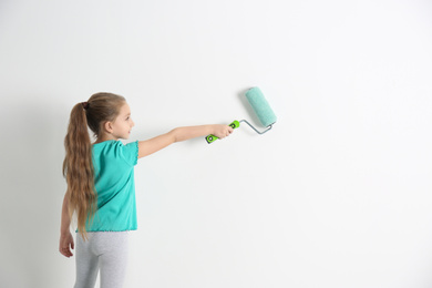 Photo of Little child painting with roller brush on white wall indoors