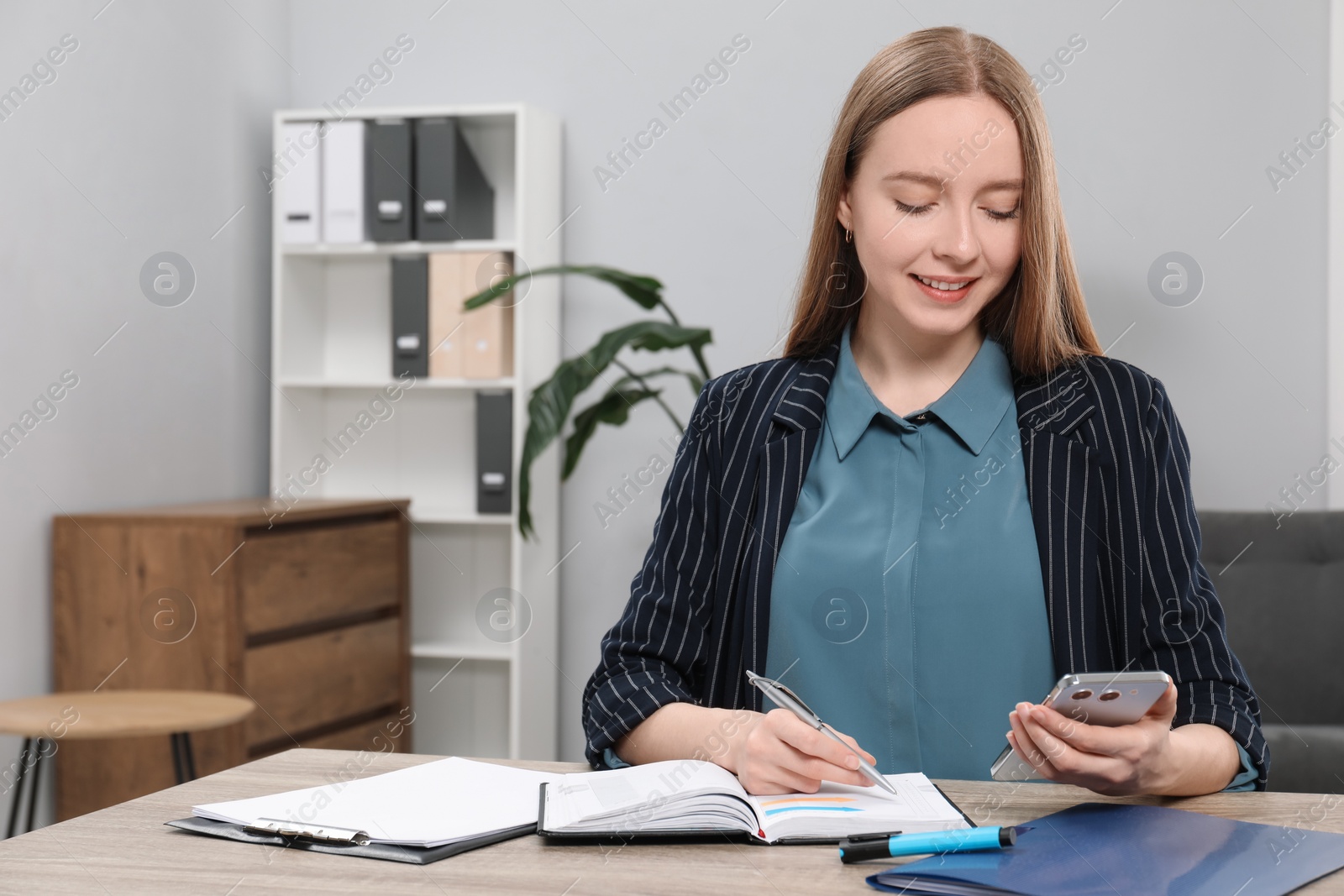 Photo of Woman taking notes while using smartphone at wooden table in office, space for text