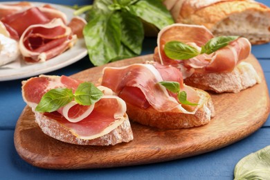 Photo of Tasty sandwiches with cured ham and basil leaves on blue wooden table, closeup