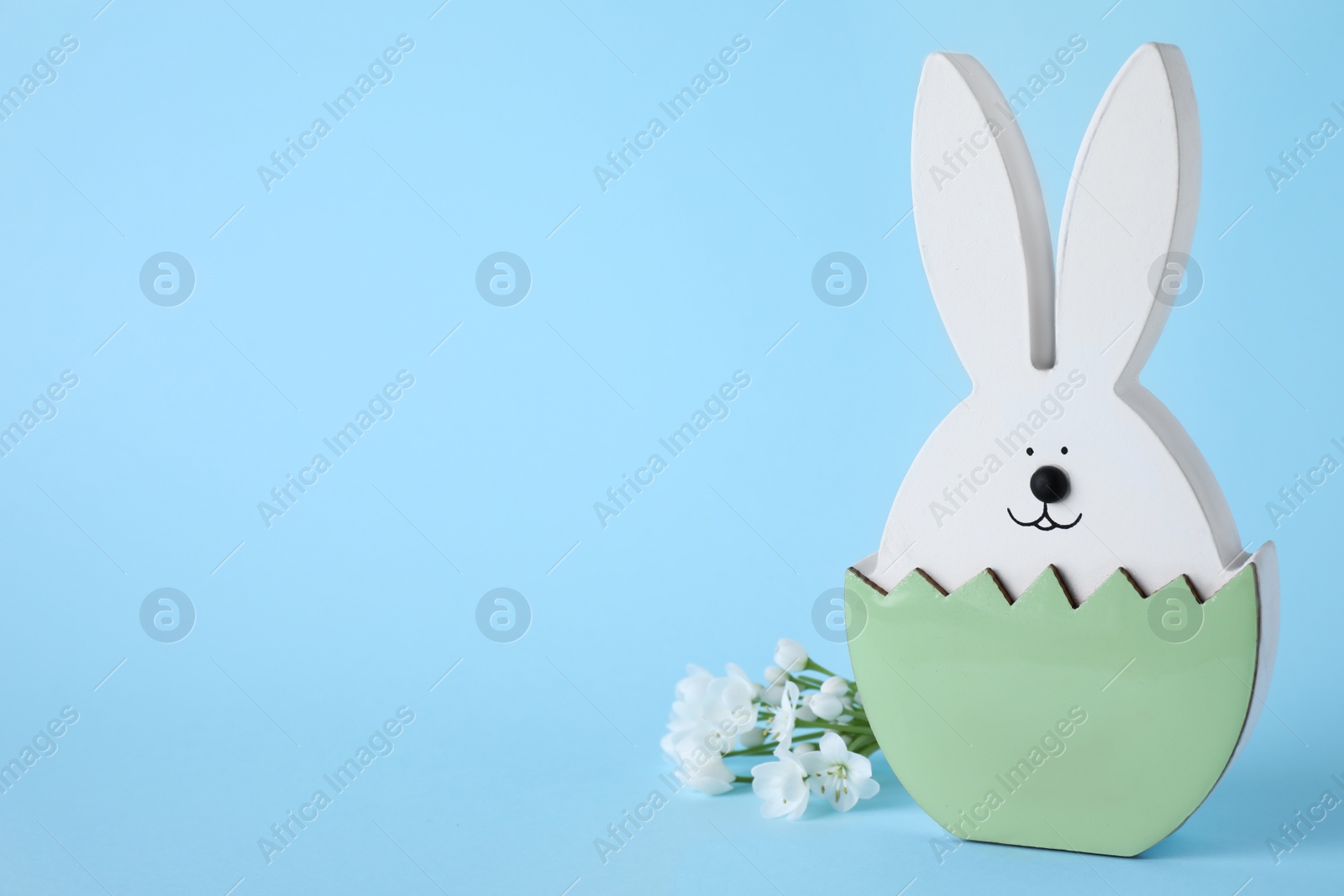 Photo of Easter bunny figure and flowers on light blue background. Space for text