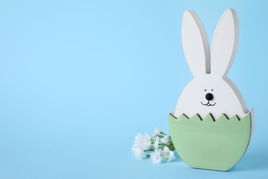 Photo of Easter bunny figure and flowers on light blue background. Space for text