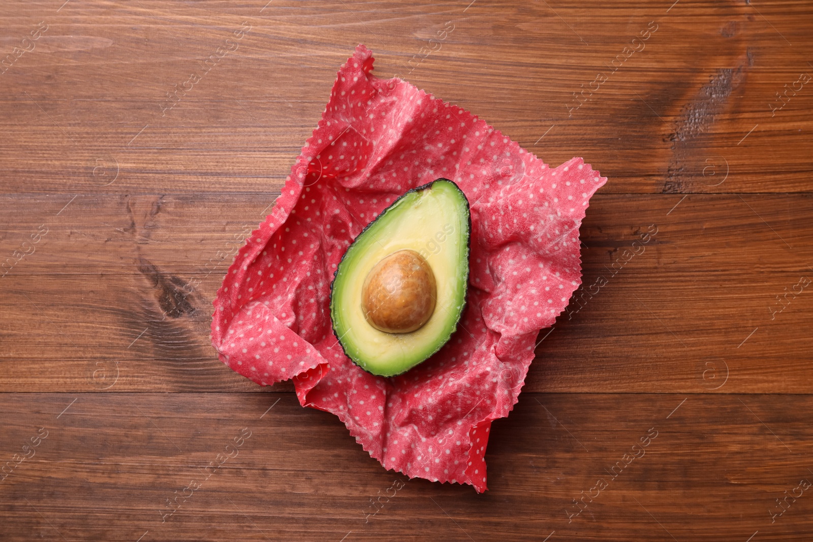 Photo of Half of avocado in beeswax food wrap on wooden table, top view