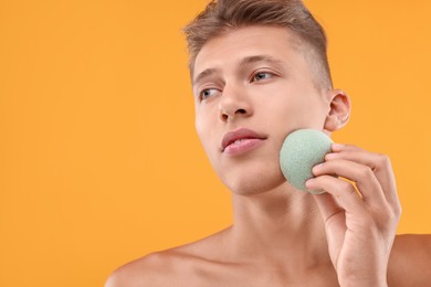 Young man washing his face with sponge on orange background. Space for text