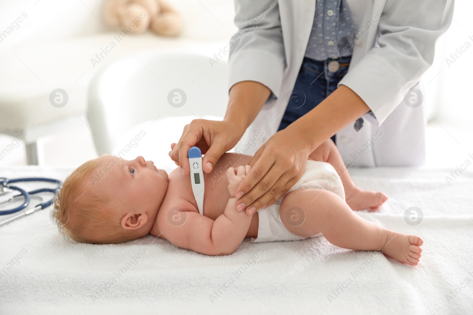 Photo of Doctor measuring temperature of little baby with digital thermometer indoors, closeup. Health care