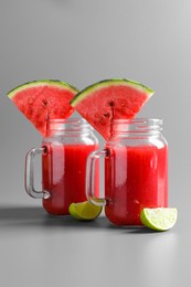 Photo of Tasty summer watermelon drink with lime in glass mason jars on grey background