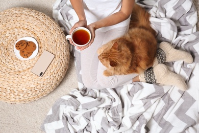 Photo of Woman with cute red cat and tea on blanket, top view