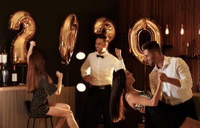 Photo of Young people celebrating New Year in club. Golden 2020 balloons on background