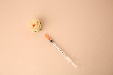 Medical syringe and beautiful rose on beige background, top view