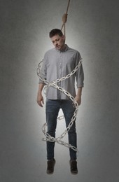 Image of Depressed man with rope noose on neck and metal chains around him against grey background