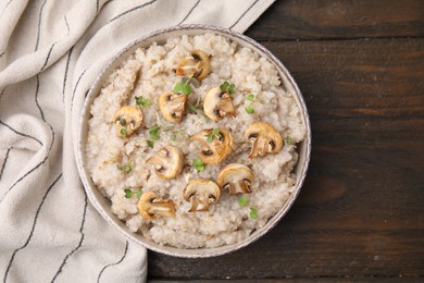 Photo of Delicious barley porridge with mushrooms and microgreens in bowl on wooden table, top view