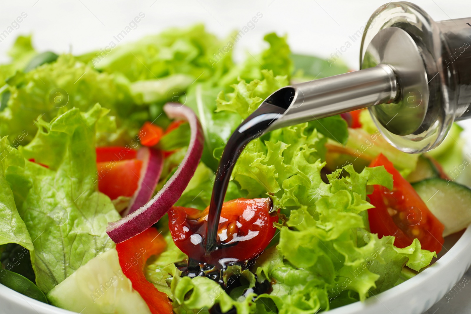 Photo of Pouring balsamic vinegar onto fresh vegetable salad in dish, closeup