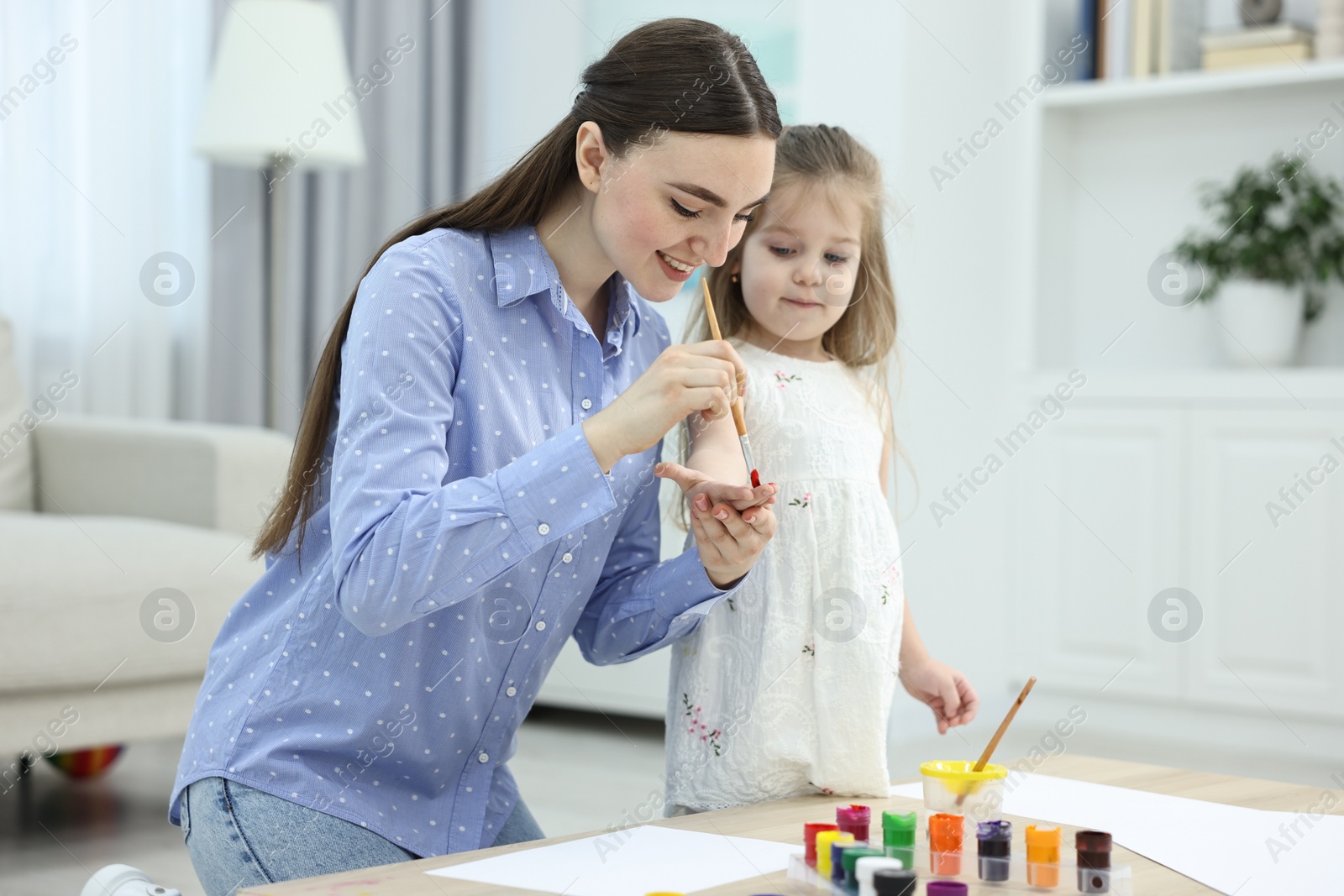 Photo of Mother and her little daughter painting with palms at home