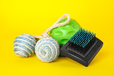 Photo of Toy balls and brush for pet on yellow background