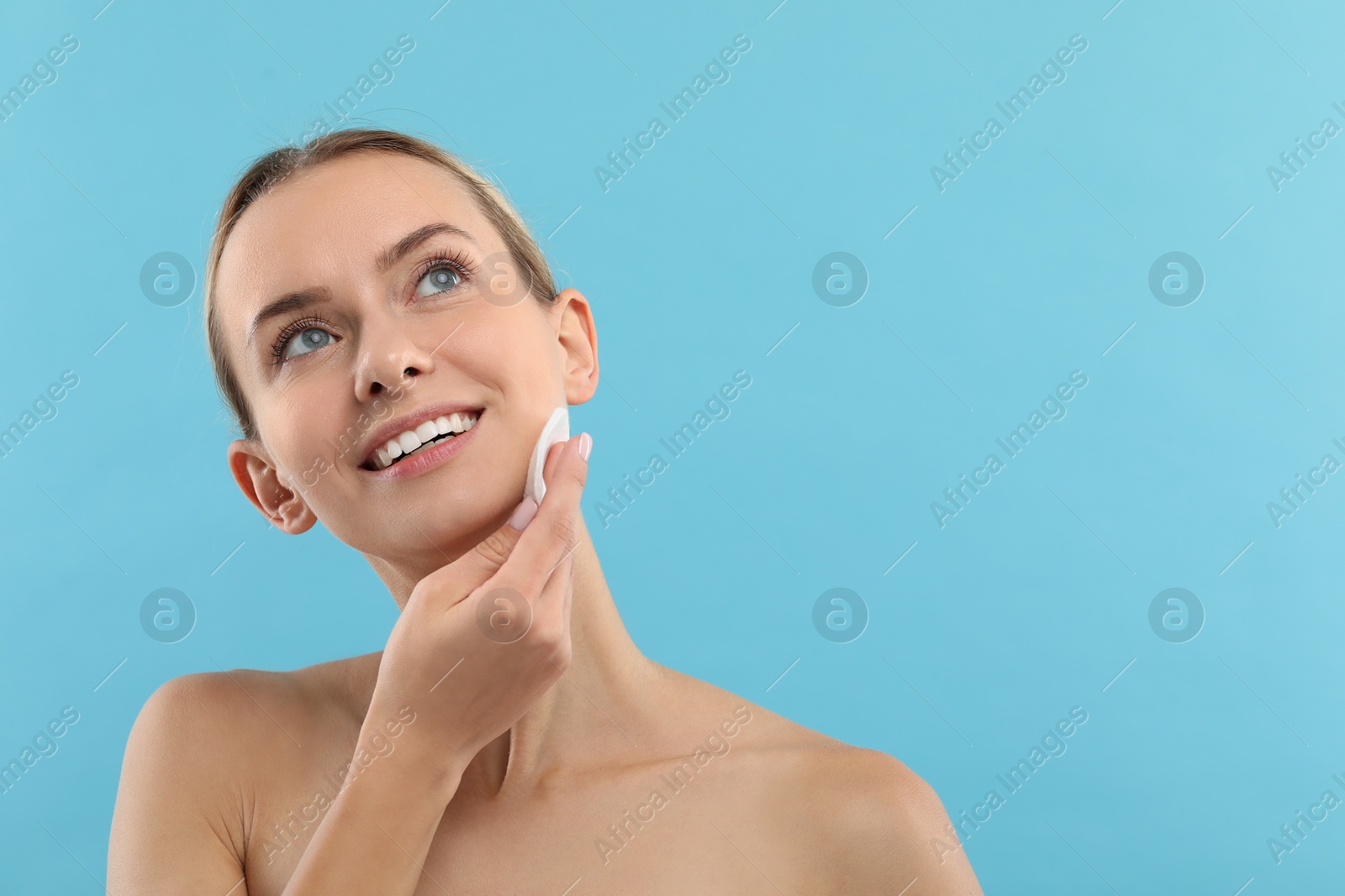 Photo of Smiling woman removing makeup with cotton pad on light blue background. Space for text