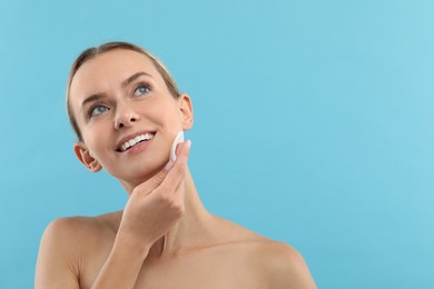 Photo of Smiling woman removing makeup with cotton pad on light blue background. Space for text