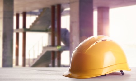 Image of Hard hat on white wooden surface at construction site with unfinished building. Space for text 