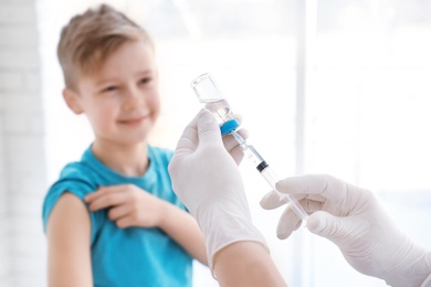 Photo of Doctor filling syringe with medicine and child on background. Vaccination day