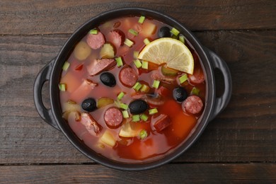 Photo of Meat solyanka soup with thin dry smoked sausages in bowl on wooden table, top view