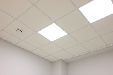 Photo of White ceiling with PVC tiles and lighting indoors, low angle view