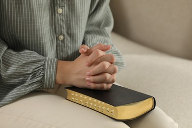 Religious woman praying over Bible on sofa, closeup