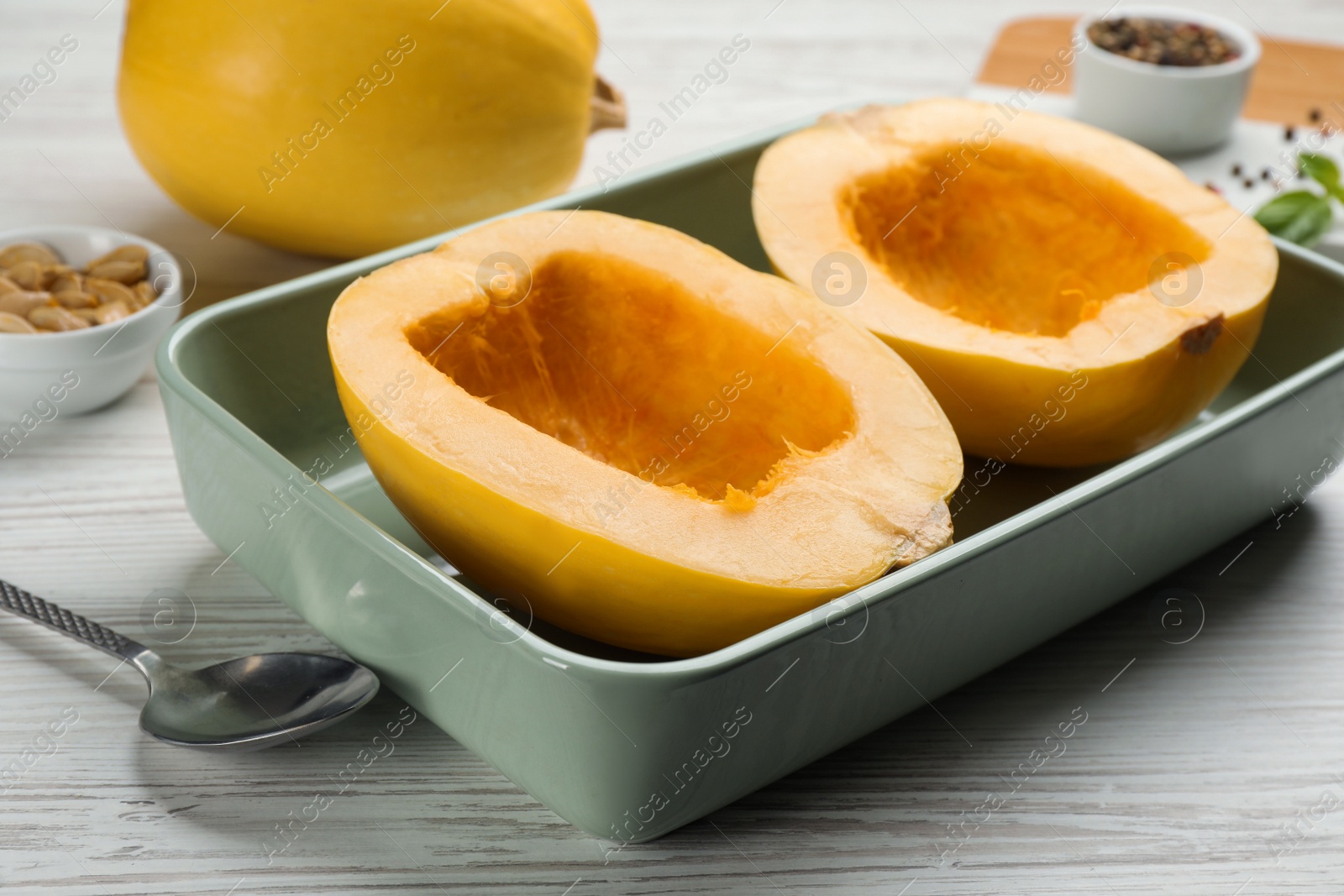 Photo of Raw spaghetti squash halves in baking dish on white wooden table, closeup