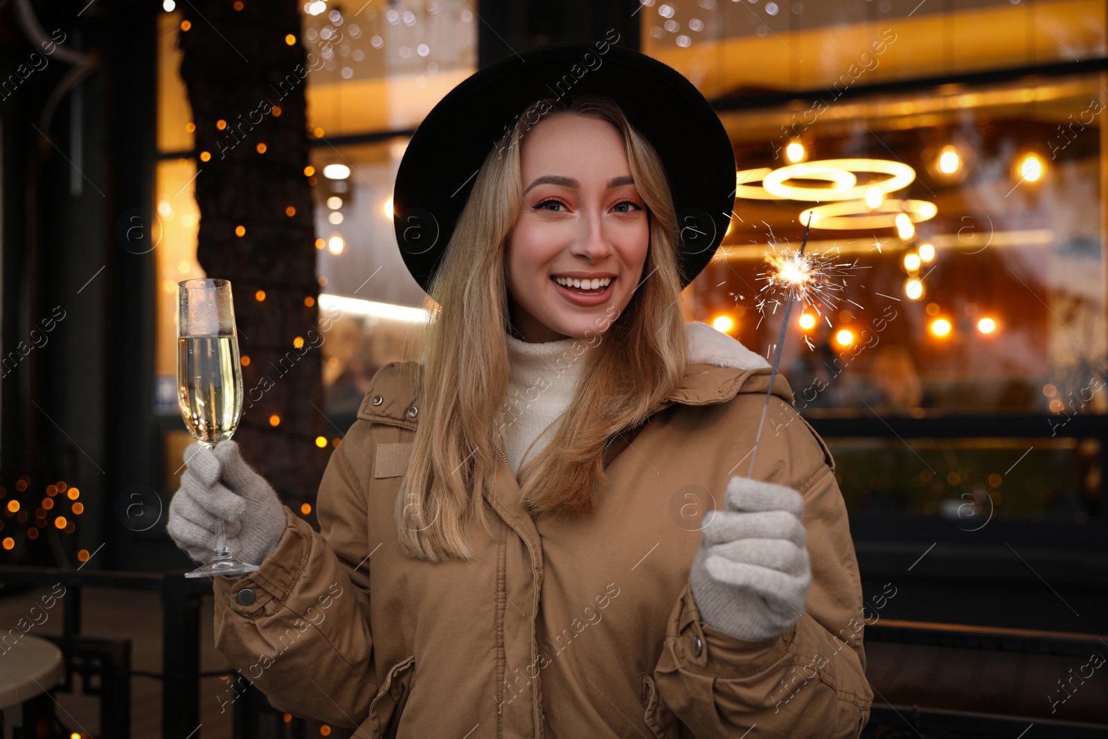 Photo of Happy young woman with sparkler and glass of champagne at winter fair