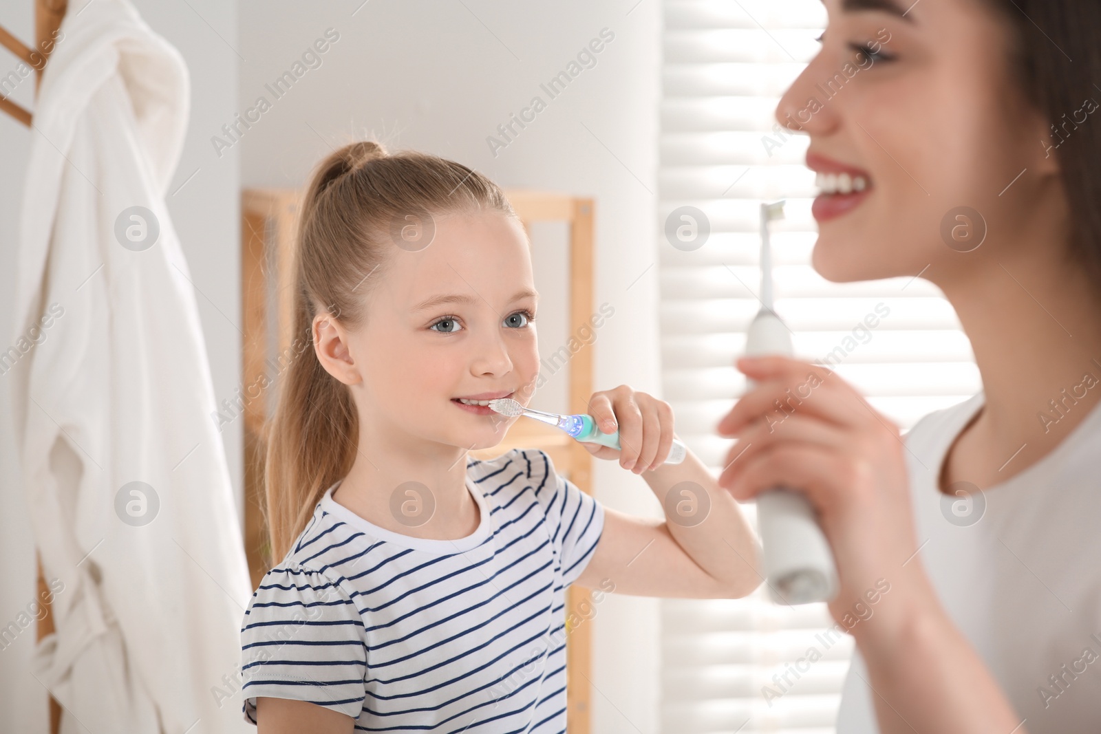 Photo of Mother and her daughter brushing teeth together in bathroom