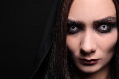 Photo of Mysterious witch with spooky eyes on black background, closeup. Space for text