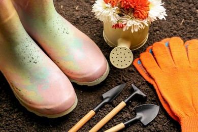 Photo of Gardening tools, gloves, boots and flowers on fresh soil