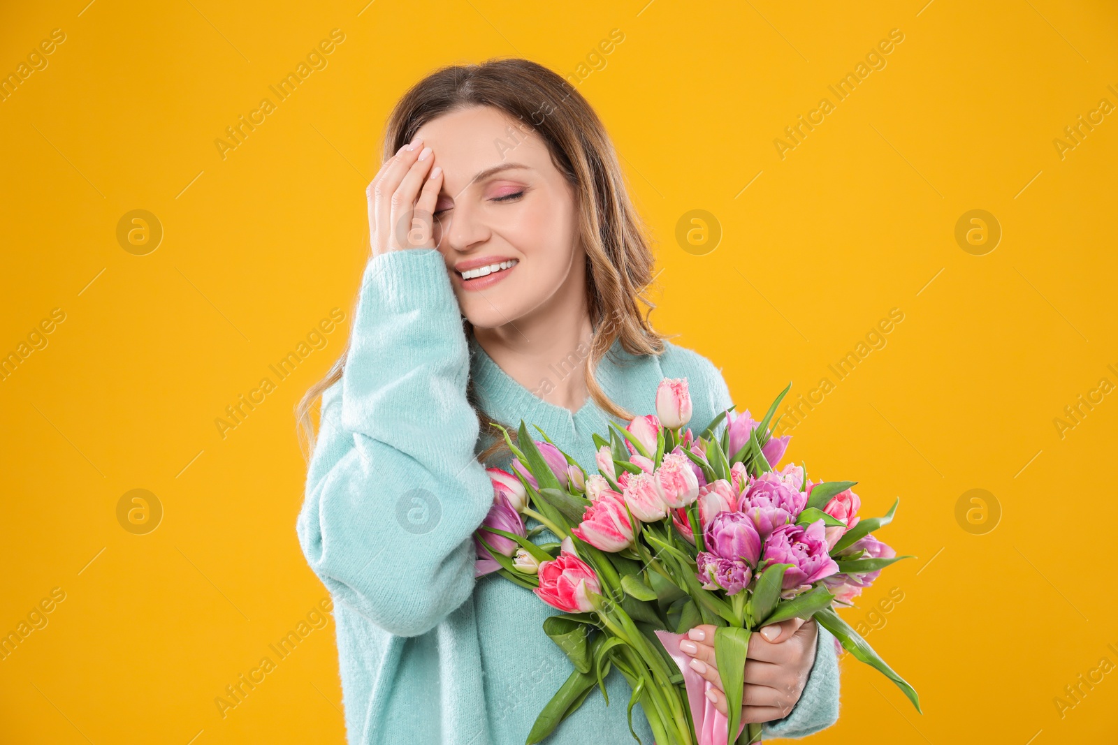 Photo of Happy young woman with bouquet of beautiful tulips on yellow background