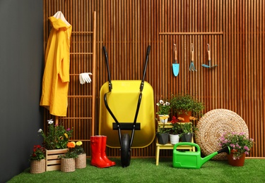 Photo of Gardening tools with wheelbarrow and flowers near wooden wall