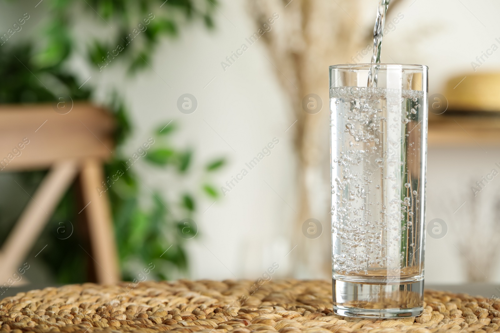 Photo of Pouring water into glass on table indoors, space for text. Refreshing drink