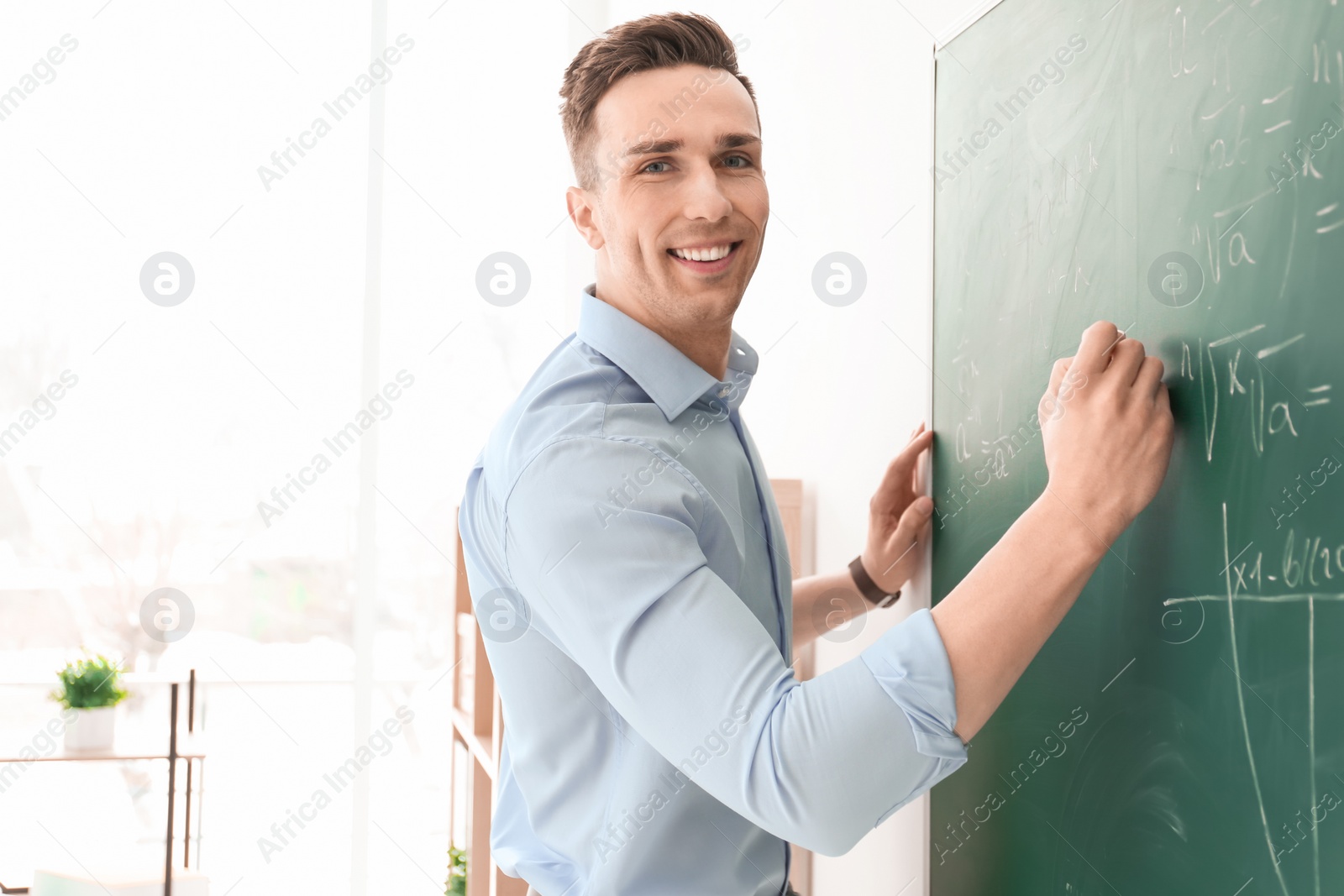 Photo of Young male teacher writing on blackboard in classroom