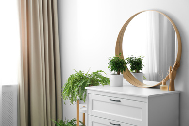 Round mirror and chest of drawers near white wall in room. Modern interior design