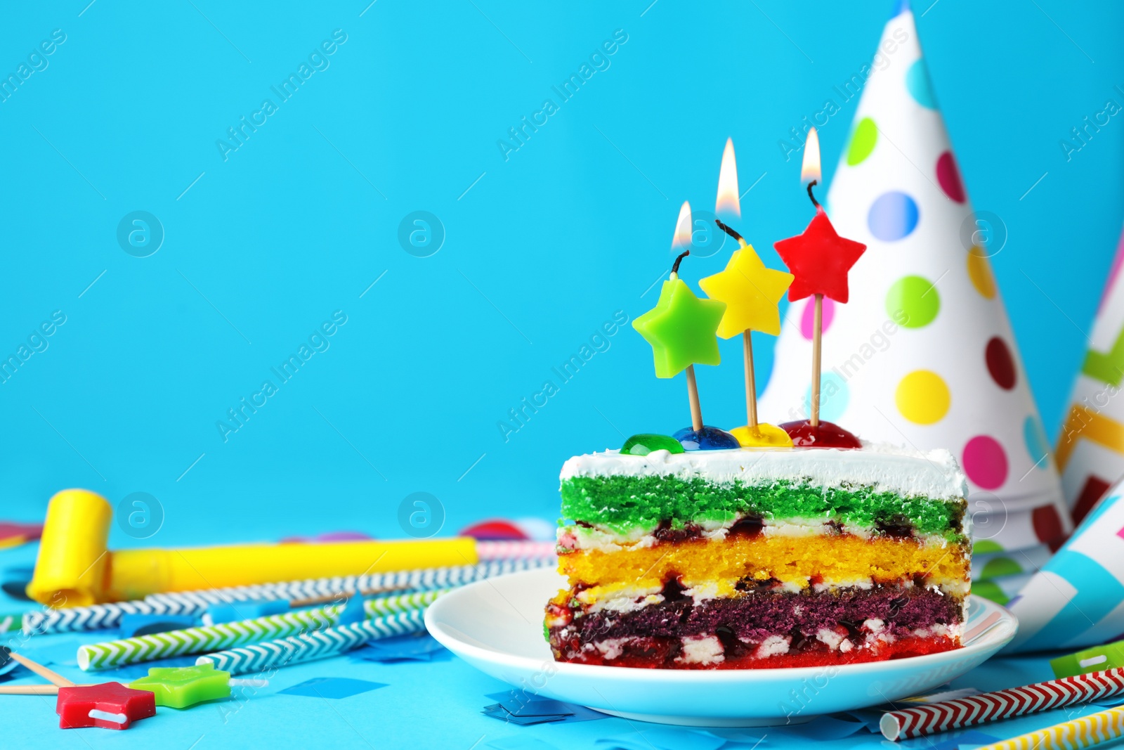 Photo of Piece of cake with candles and birthday decor on light blue background, space for text