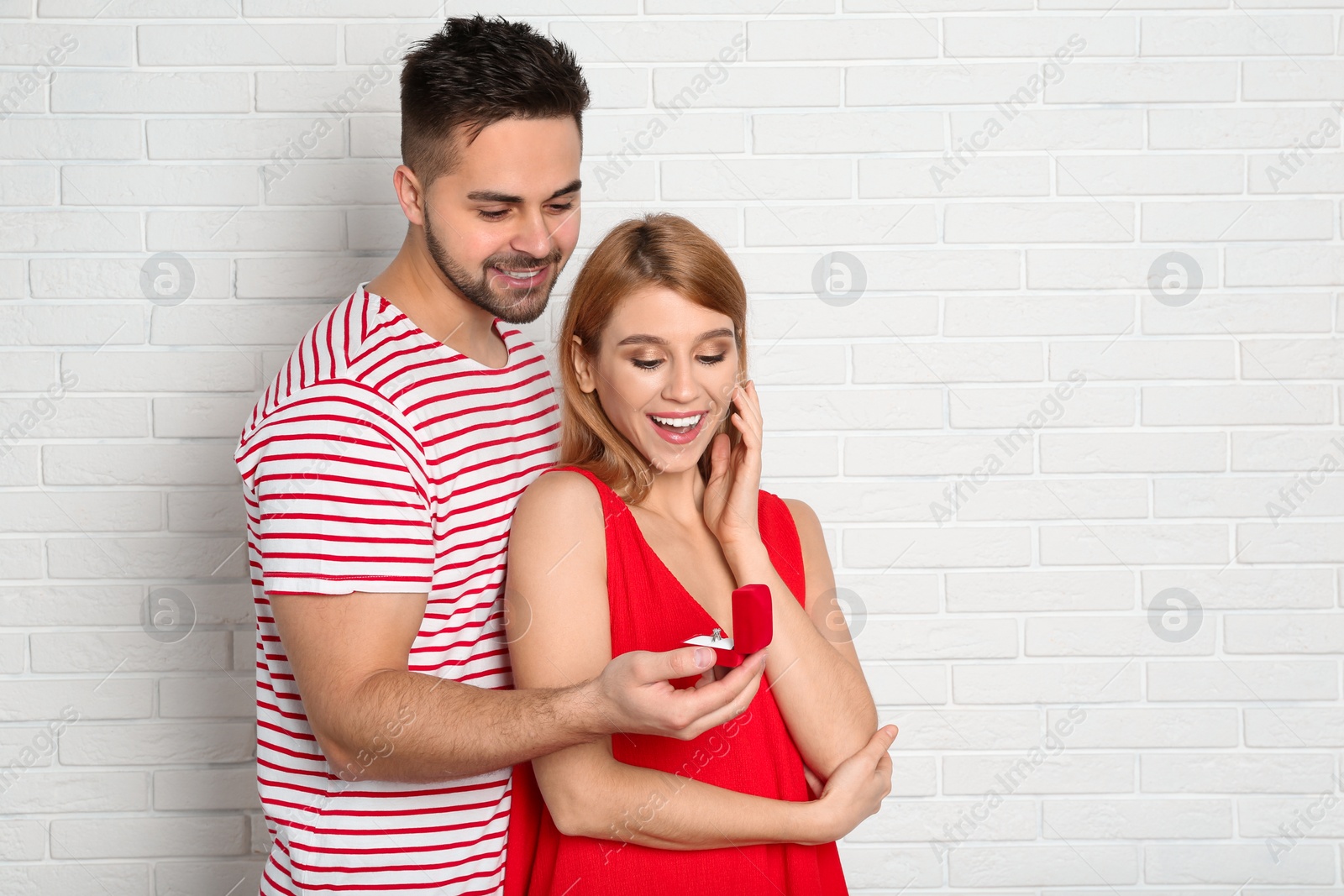 Photo of Man with engagement ring making marriage proposal to girlfriend near white brick wall. Space for text