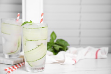 Glasses of refreshing cucumber water with basil on white table, space for text