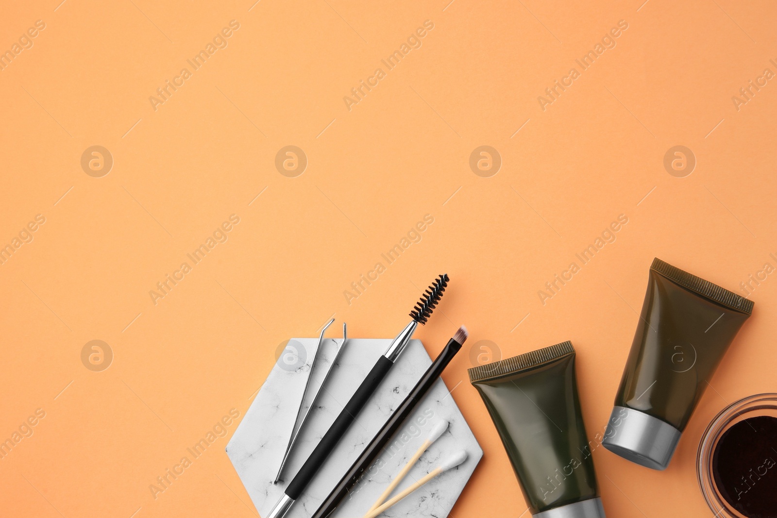 Photo of Flat lay composition with eyebrow henna, professional tools and cosmetic products on orange background, space for text