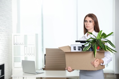 Upset young woman carrying box with stuff at office