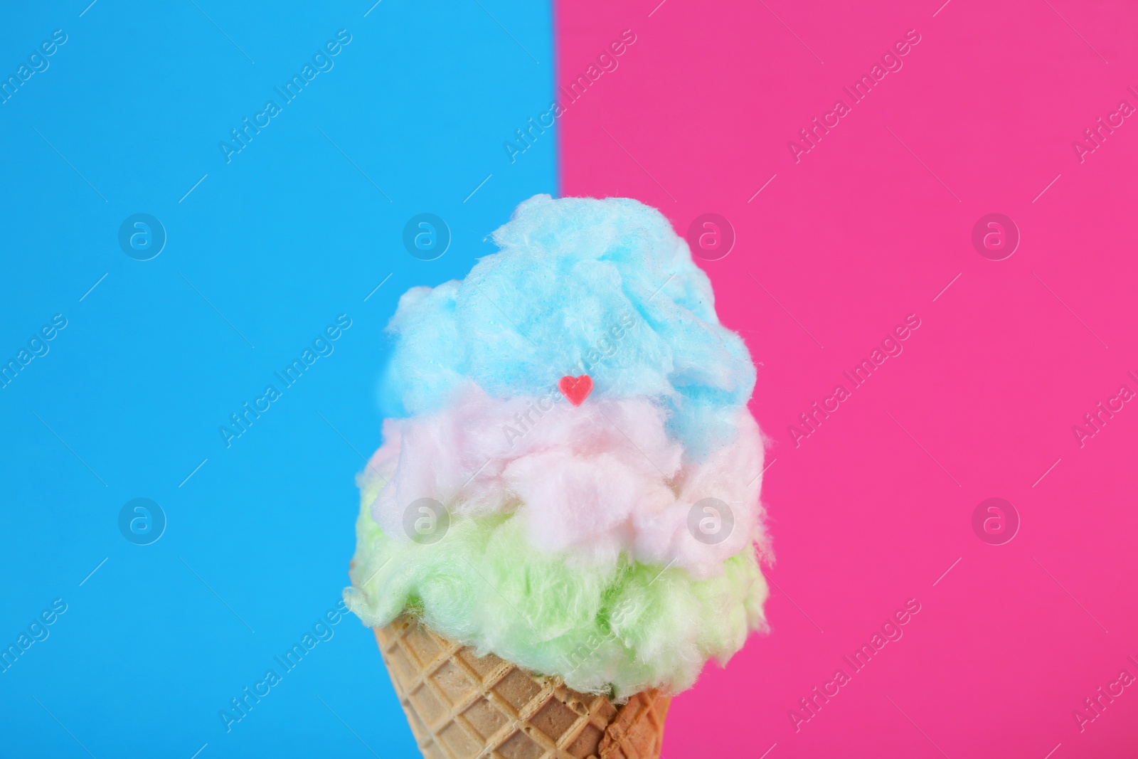 Photo of Sweet cotton candy in waffle cone on color background, closeup