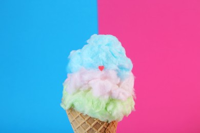 Sweet cotton candy in waffle cone on color background, closeup