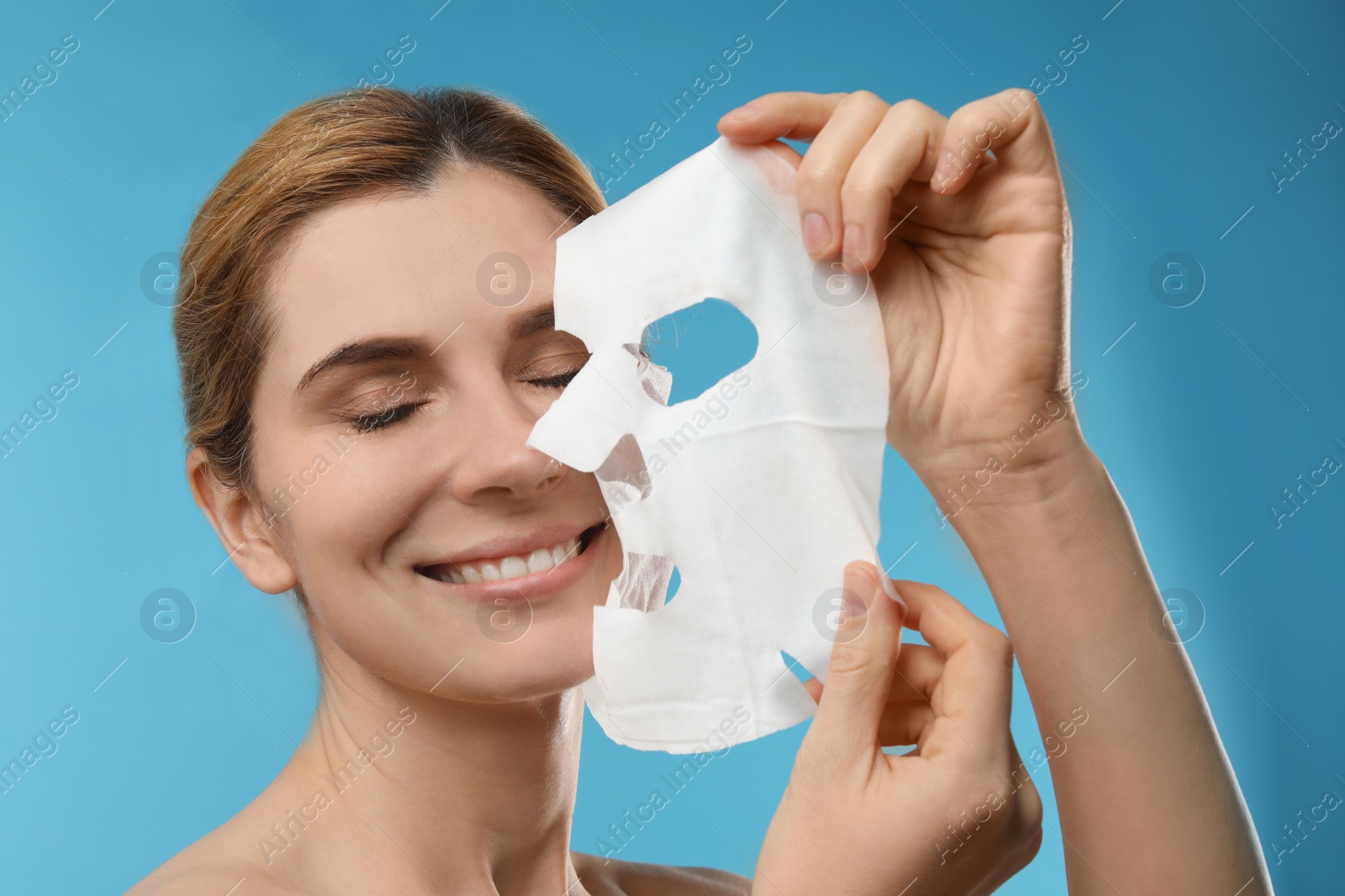 Photo of Beautiful woman with cotton facial mask sheet against color background