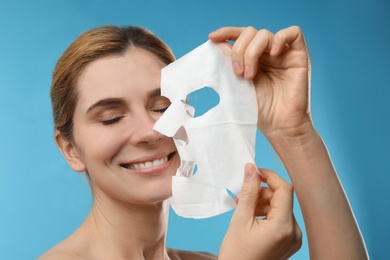 Photo of Beautiful woman with cotton facial mask sheet against color background