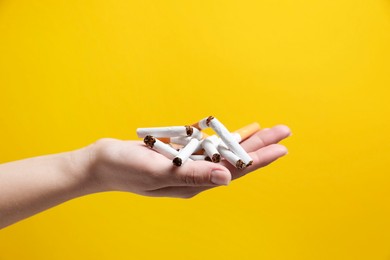 Photo of Stop smoking. Woman holding broken cigarettes on yellow background, closeup