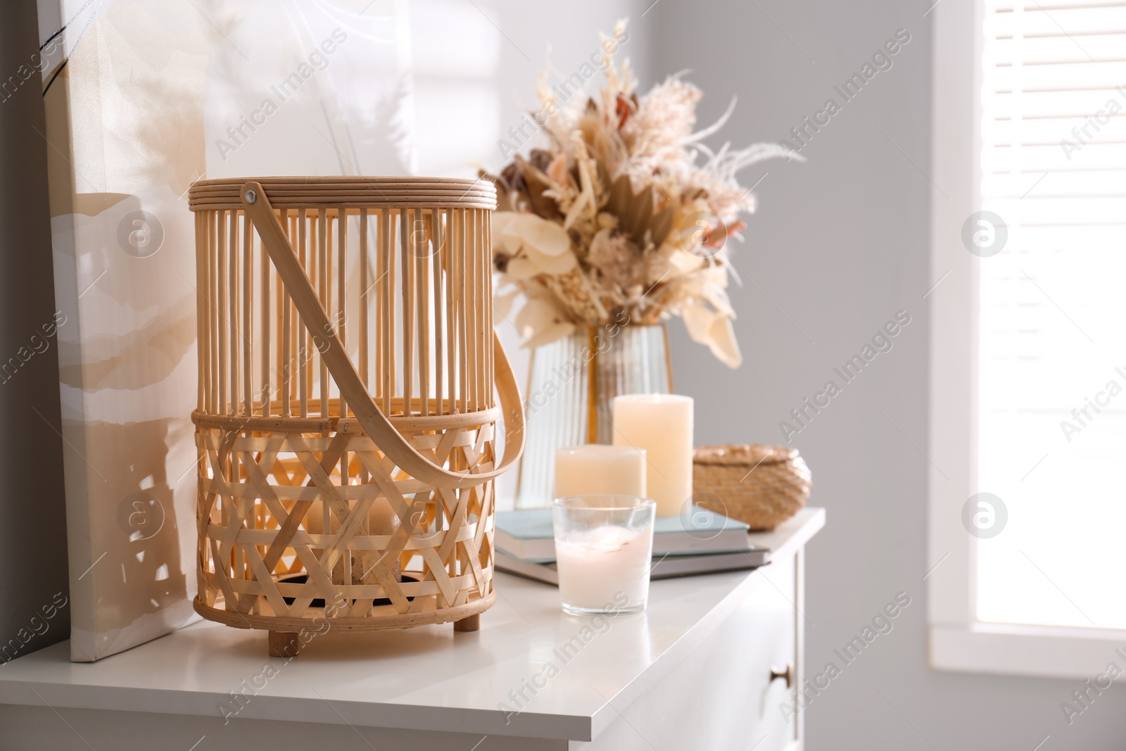 Photo of Burning scented candles and bouquet on white chest of drawers in room