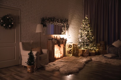 Stylish interior with beautiful Christmas tree and artificial fireplace at night