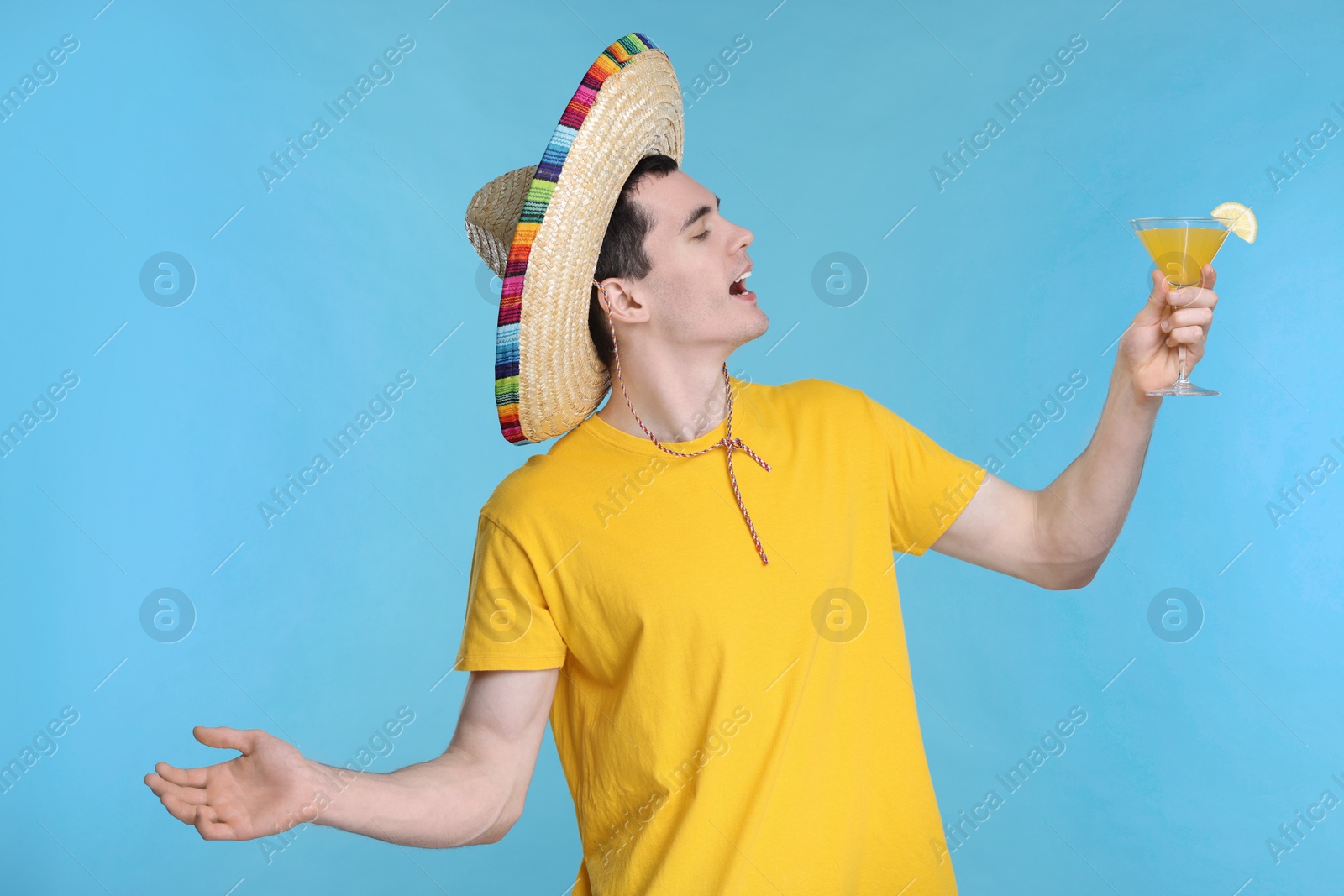 Photo of Young man in Mexican sombrero hat with cocktail on light blue background